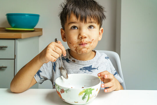 Little boy with chocolate on face eats his pudding very enjoyable