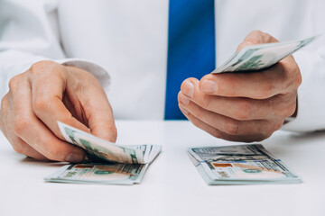 close-up of men's hands counting a stack of hundred-dollar US banknotes. a businessman in a white shirt counts cash. the concept of investment, money exchange, bribes or corruption. selective focus.