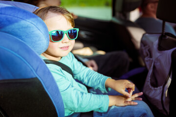 Toddler boy weraing sun glasses sitting in a car seat, family travelling by car. Preschool child in the auto.