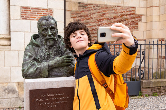Teenager boy taking a selfie with a monument, making funny content for social media. Travelling student, sightseeing.