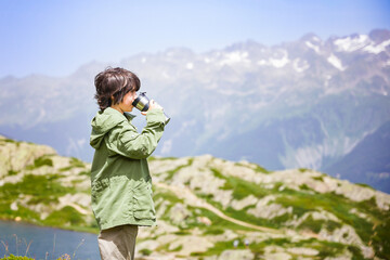 Young boy doing hiking, staying in a mountains, holding travel tumbler and drinking tea.