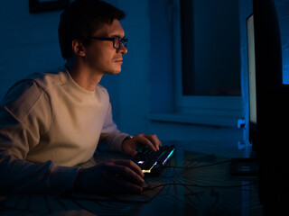 The male programmer works late. A guy with glasses is sitting in a dark office in front of a...