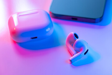 Modern luxury wireless earphones, case for white headphones storage and charging, new phone on neon background