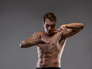 A muscular man expressively emotionally poses on a gray background. The guy is an athlete with pumped-up muscles. beautiful body relief. © Ulia Koltyrina