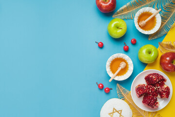 Jewish holiday Rosh Hashana banner design with honey, apple and pomegranate over blue background. Top view, flat lay