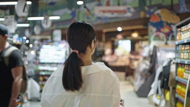 Busy woman walks past racks searching goods in supermarket