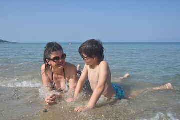 Happy family enjoy at beach. Summer vacation, smiling and joy in water. Mom with the small son on beach in the sea waves