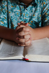 A person holding his hands, praying to God on the Bible. 