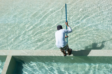 Rear view shot from above of a maintenance worker cleaning a pool with a brush in Mexico