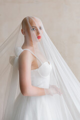 Fototapeta na wymiar Bald beautiful bride in a luxurious wedding dress in red lipstick and a long veil is sick with cancer