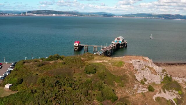 Aerial View of Mumbles Lighthouse and Pier, part of the Gower coastline in South Wales. bright blue waters on a sunny summers day. parallax effect rasing over small mountain terain