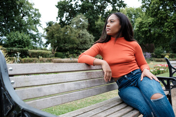 Portrait of serious young mixed race woman sitting on a bench on a park and looking away.
