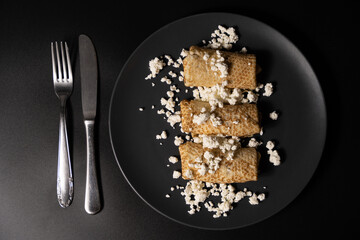 pancakes with cheese on a plate and kitchen utensils on a black background