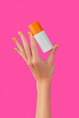Manicured womans hand holding sunscreen bottle on pink background