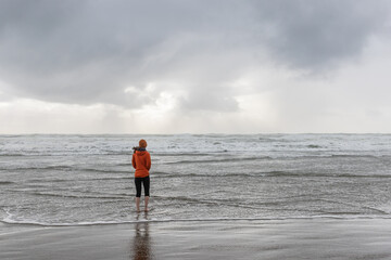 Girl walks in orange coat and hat along the oregon coast during a cold rainy day 