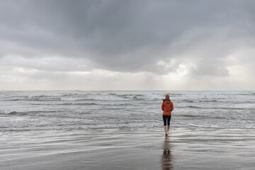 Girl walks in orange coat and hat along the oregon coast during a cold rainy day 