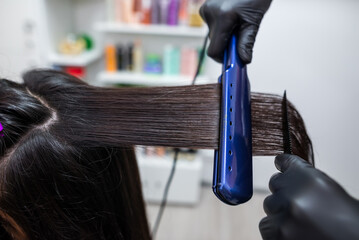 Hairdresser using a hair straightened to straighten the hair. Hair stylist working on a woman's...