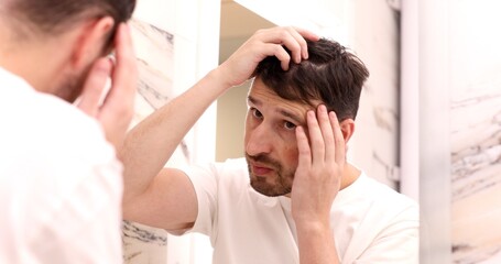 Hair loss man looking in bathroom mirror putting wax touching his hair styling or checking for hair...