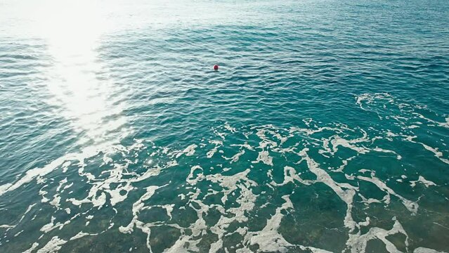 A little red buoy floats and waving in blue ocean water in the early morning, marking fish trawling area spot