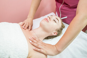 Obraz na płótnie Canvas female masseuse massaging the shoulders and arms of a young woman lying with her eyes closed on the couch