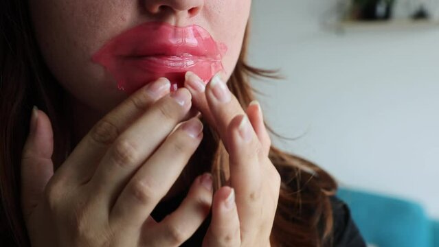 Woman using collagen lip mask for dry and chapped lips. Girl puts on a red mask to respect lips. Beauty routine at home. Pink hydrogel lips patch. Korean cosmetics.