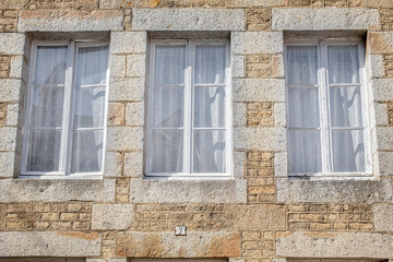 Detail of an old French Normandy house with three windows and closed curtains