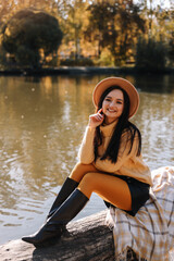 A smiling beautiful young woman in a fashionable hat and casual clothes enjoys a walk alone in an fall park in the autumn outdoors. Selective focus