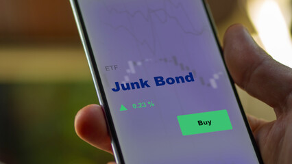 An investor's analyzing the junk bond etf fund on a screen. A phone shows the prices of Junk-Bond
