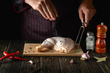 The cook adds salt to the chicken leg. Grilled blank with chicken ham in the kitchen of a restaurant or hotel on a table with spices