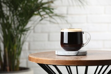 Glass mug of coffee with stylish stone cup coaster on wooden table in room. Space for text