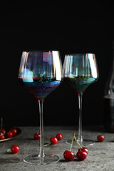 Delicious cherry wine with ripe juicy berries on grey table against black background