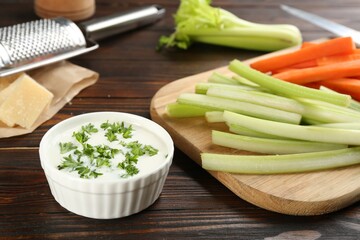 Celery and carrot sticks with dip sauce on wooden table, closeup
