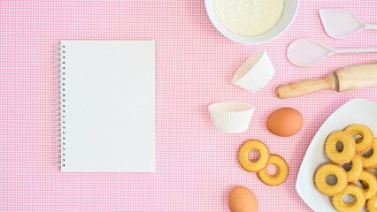 Fototapeta na wymiar ingredients for preparing cookies on pastel pink background with notebook for recipe. Flat lay