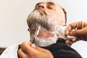Barber trimming and cutting bearded man with shaving machine in barbershop. Hairstyling process.