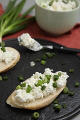Bread with cottage cheese and green onion on slate board, closeup