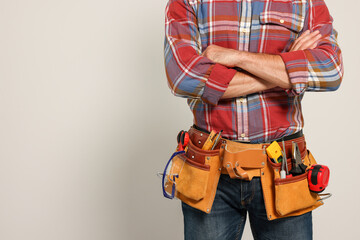 Fototapeta premium Professional builder with tool belt on light background, closeup. Space for text