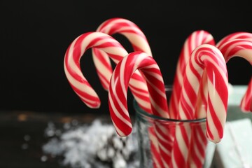 Many sweet candy canes in glass on black background, closeup. Traditional Christmas treat