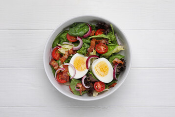 Delicious salad with boiled egg, bacon and vegetables on white wooden table, top view