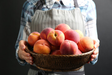 Woman with fresh sweet peaches in wicker bowl, closeup