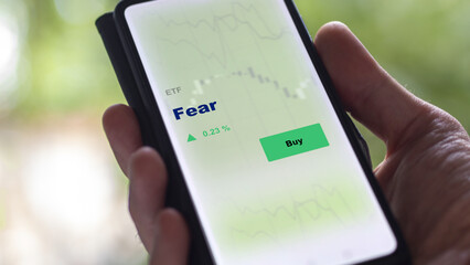 An investor's analyzing the fear etf fund on screen. A phone shows the fear ETF's prices to invest.