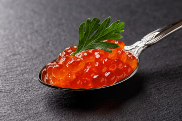 Salmon red caviar and parsley in a spoon macro. Vintage spoon full of trout caviar over black slate...