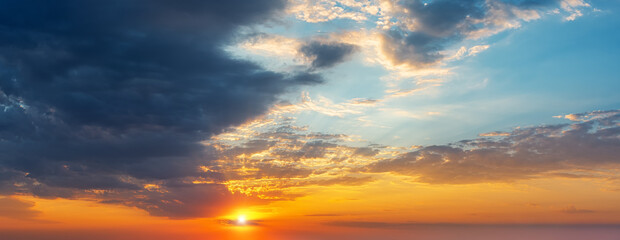 Setting sun in the orange blue evening sky. Sun rays break through the light clouds at sunset. Dark...