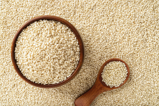 Raw sesame seeds in a wooden bowl and spoon over white til background. Organic benne grains for healthy food,  boosting immunity diet and calcium source. Sesamum indicum crop. Asian cuisine.