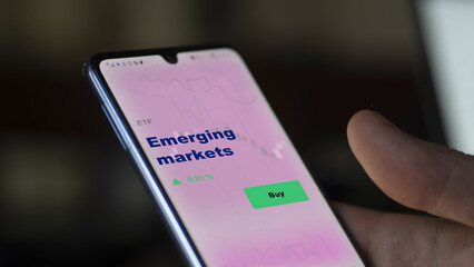 An investor's analyzing the emerging markets etf fund on screen. A phone shows the emerging markets ETF's to invest