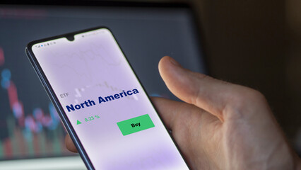An investor's analyzing the north america etf fund on screen. A phone shows the North America ETF's prices petrol and gasoline energy to invest