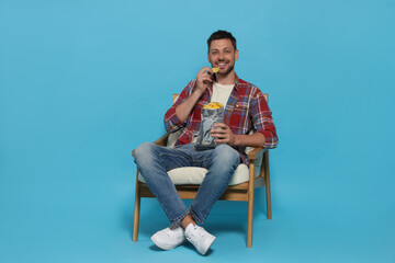 Handsome man eating potato chips on light blue background