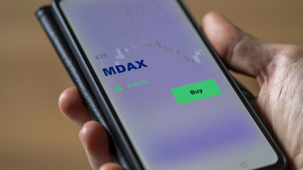 An investor's analyzing the MDAX etf fund on screen. A phone shows the ETF's prices mdax to invest