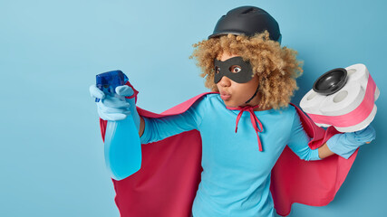 Impressed shocked curly haired woman pretends being superhero holds bottle of spray detergent and...