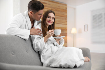 Obraz na płótnie Canvas Man in bathrobe hugging his girlfriend with coffee at home