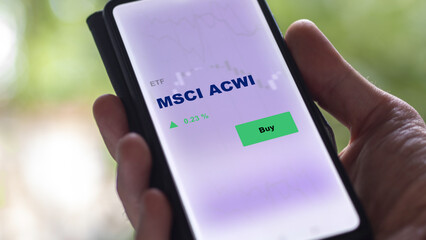 An investor's analyzing the MSCI ACWI etf fund on screen. A phone shows the ETF's prices msci acwi to invest